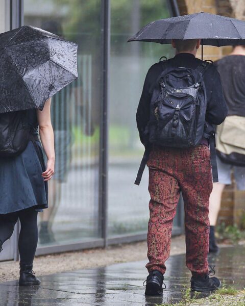Personen mit Regenschirmen unter einem bewölkten Himmel, symbolisieren wechselhaftes Frühlingswetter in Niedersachsen.