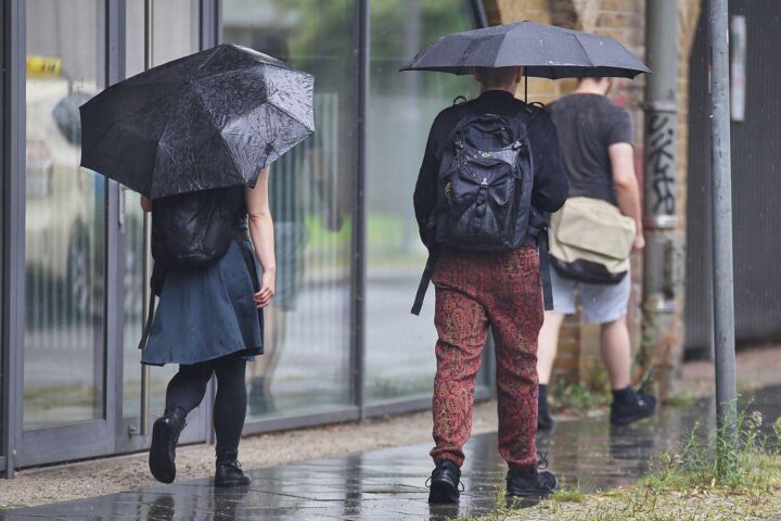 Personen mit Regenschirmen unter einem bewölkten Himmel, symbolisieren wechselhaftes Frühlingswetter in Niedersachsen.