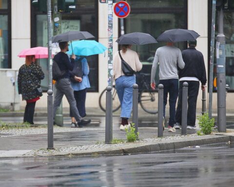 Personen mit Regenschirmen unter bewölktem Himmel in Nordrhein-Westfalen. Milder Regen vorausgesagt.