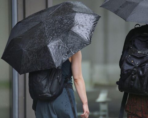 Ein nasser Regenschirm, umgeben von grauem, bewölktem Himmel und fallendem Regen.