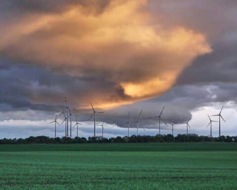 Windräder vor wolkig-blauem Himmel, symbolisieren den Einfluss von Wetter und erneuerbarer Energie.