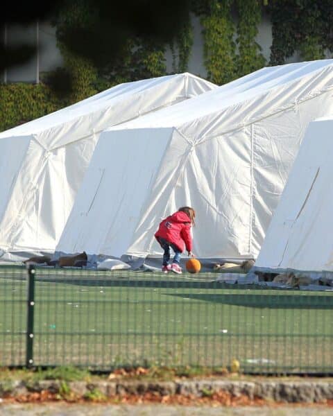 Ein Flüchtlingskind in einer Zeltstadt, das Hoffnung und Unsicherheit symbolisiert.