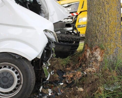 Unfallfahrzeug am Baum, Rettungsdienste und beschädigter Transporter nach schwerem Verkehrsunfall.
