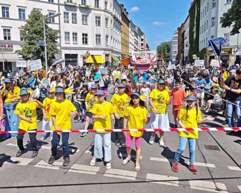 Bunt gekleidete Kinder feiern Karneval, während sie für Umweltschutz und Bildung demonstrieren.