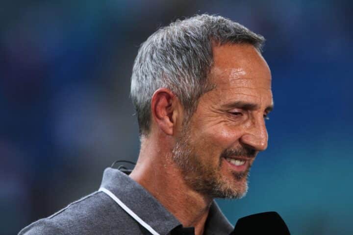 Adi Hütter, Eintracht Frankfurt Trainer, jubelnd auf dem Spielfeld, umgeben von Spielern und Fans.