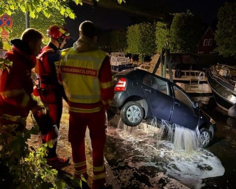 Abschleppwagen mit Kran hebt versunkenes Auto aus Auricher Hafenbecken. Feuerwehr und Rettungsdienst präsent.
