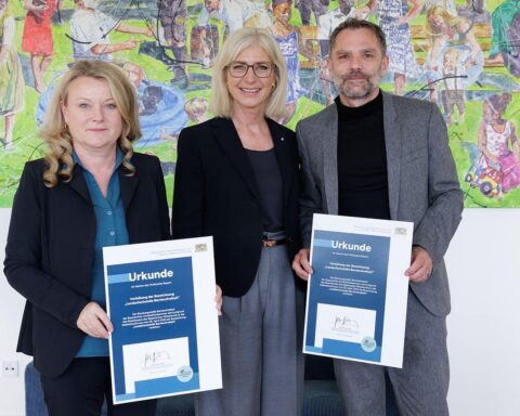 Ulrike Scharf übergibt Prädikat „Landesfachstelle Barrierefreiheit“ an Architektenkammer-Vertreter in München.