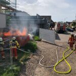 Feuerwehr löscht brennende Mulde, Notfalleinsätze nach Unwetter, entwurzelter Baum behindert Straßenverkehr.