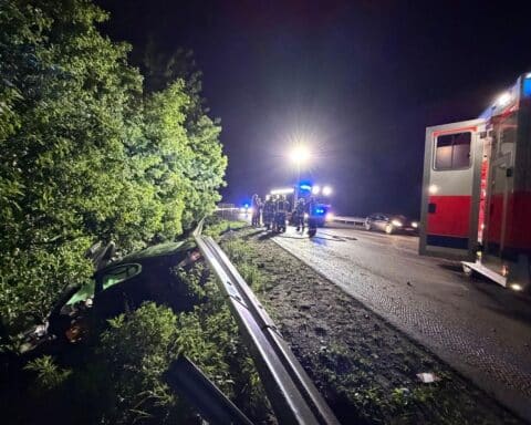 PKW im Graben hinter Leitplanke, Feuerwehr und Ersthelfer an Unfallstelle aktiv.