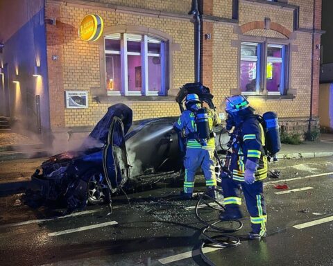 Feuerwehr löscht Pkw-Brand, Einsatzkräfte unter Atemschutz, Gefahr für angrenzendes Gebäude.