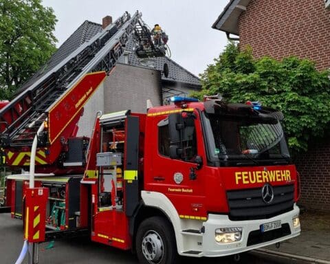 Feuerwehrleute löschen Brand in Balkon eines Mehrfamilienhauses, Bewohnerin erleidet Rauchgasvergiftung.