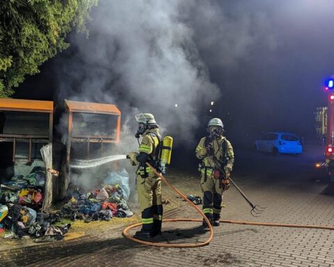 Brennende Altkleidercontainer bei Nacht, Feuerwehrleute löschen Flammen, dramatische Einsatzszene in Xanten.