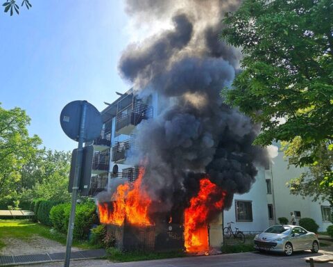 Feuerwehrleute löschen Brand an Gebäude, starker Rauch, Unterstand betroffen, Sicherheit der Bewohner gewährleistet.