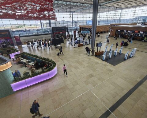Flughafen Berlin Brandenburg mit Passagieren, leeren Terminals und abfliegenden Flugzeugen im Hintergrund.