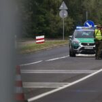 Zwei Grenzbeamte kontrollieren Fahrzeuge an der deutschen-polnischen Grenze, symbolisieren kontroverse Grenzpolitik.