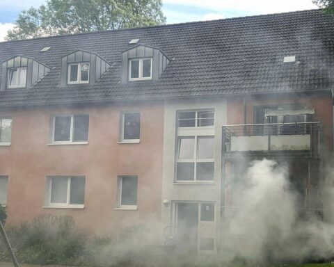 Einsatzkräfte löschen Kellerbrand in Mehrfamilienhaus, Bewohner sicher evakuiert, Rauch dringt nach draußen.