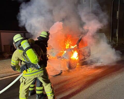 Brennender Kleintransporter am Fahrbahnrand, Feuerwehr im Einsatz mit Löschschaum.