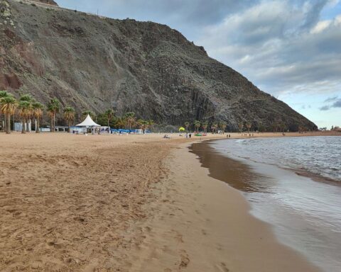 Weißer Sandstrand auf Teneriffa, unberührte Küste, Sicherheitsmaßnahmen und Kreuzfahrtschiff im Hintergrund.