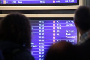 Passagiere am Frankfurter Flughafen warten vor einer großen Informationstafel für Flüge.