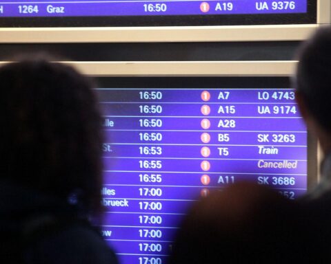 Passagiere am Frankfurter Flughafen warten vor einer großen Informationstafel für Flüge.