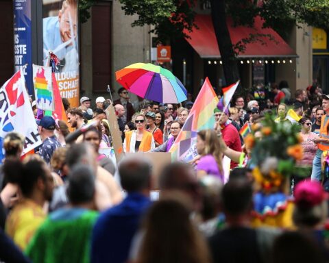 Bunte Parade mit Menschen in Regenbogenfarben, die Vielfalt und Solidarität der queeren Community feiern.