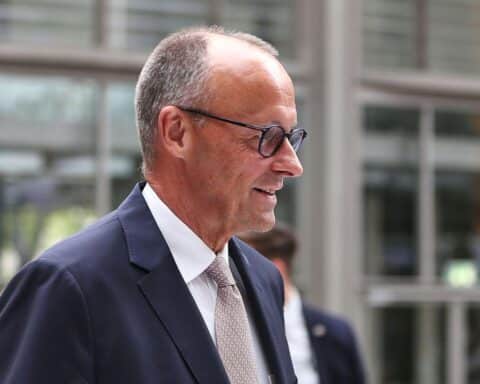 Friedrich Merz im Vordergrund, im Hintergrund Koalitionsgespräche zwischen Union und SPD skizziert.