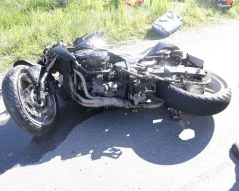 Motorrad schwer beschädigt nach Unfall, Abschlepper vor Ort, Feuerwehr reinigt Fahrbahn.