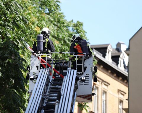 Feuerwehrleute löschen Mülltonnenbrand in Garage, sichern Umgebung, Wärmebildkamera im Einsatz.