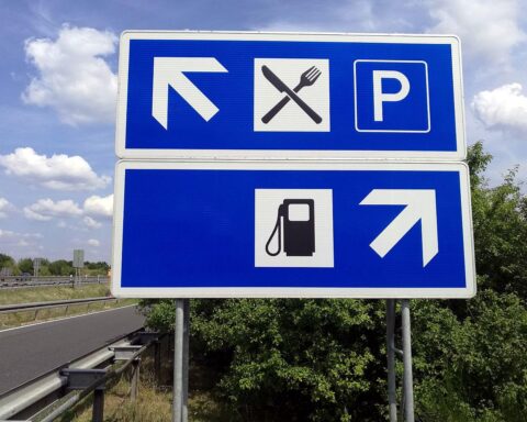 Tankstelle mit Preisanzeigen, spritpreisändernde Schilder, Menschen, die tanken, während der 12-Uhr-Regel.