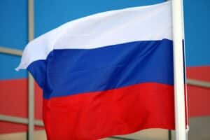 Russische Fahne vor einem Hintergrund, der militärische Konflikte und Spannungen symbolisiert.