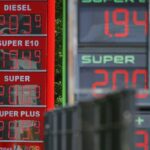 Tankstelle mit Zapfsäulen, Fahrer schaut besorgt auf Preisschilder, symbolisiert aktuelle Preiserhöhung und Politik.
