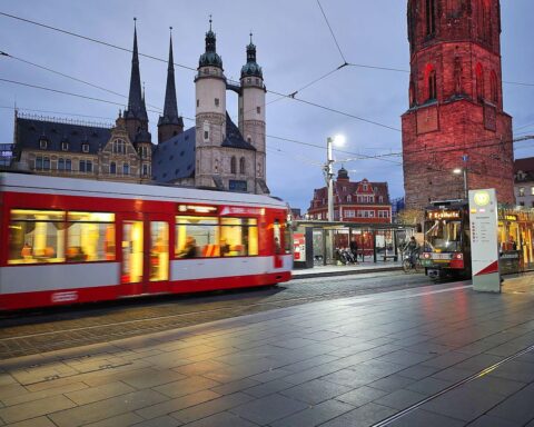 Straßenbahn auf dem Marktplatz, umgeben von steinernen Flächen, symbolisiert zukünftige Baumpflanzungen.