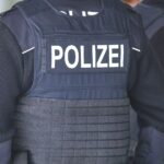 Ein trauriges Autobild mit einer Polizeiabsperrung und einem Krankenwagen im Hintergrund.