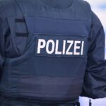 Eine verletzte Frau auf einem Waldweg, Fahrrad neben ihr, Polizei und Rettungswagen im Hintergrund.