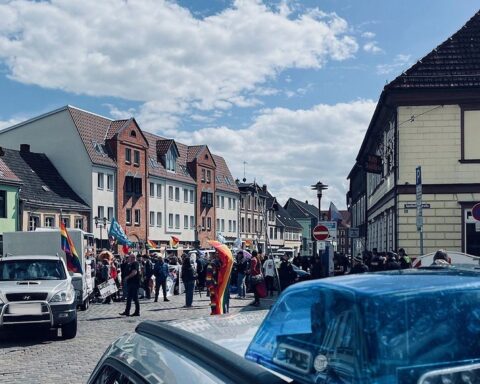 Friedliche Versammlung mit bunten Fahnen und Menschen, Polizei im Hintergrund überwacht das Geschehen.