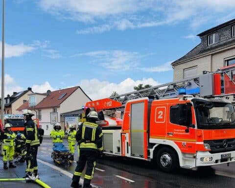 Einsatzkräfte löschen Brand in Wohngebäude; eine Person verstorben, Straße gesperrt.