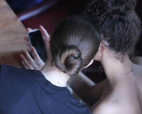 Junge Frauen diskutieren am Smartphone über KI-Inhalte und deren Regulierung auf digitalen Plattformen.