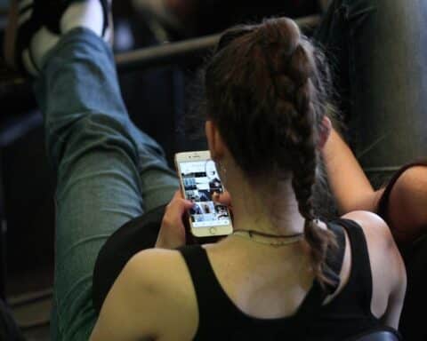 Junge Frau sieht skeptisch auf Smartphone, symbolisiert Unsicherheit über Fake News und Desinformation.