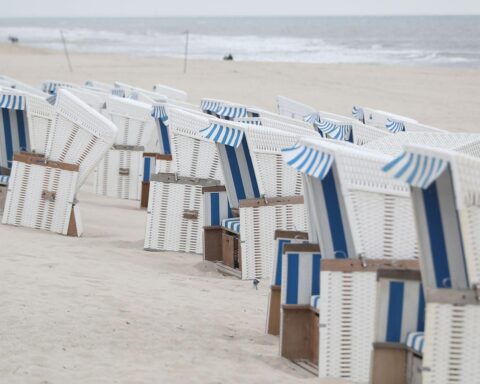 Strandkörbe am Strand unter wechselhaftem Wetter mit Regen und Gewitterwarnung im Hintergrund.