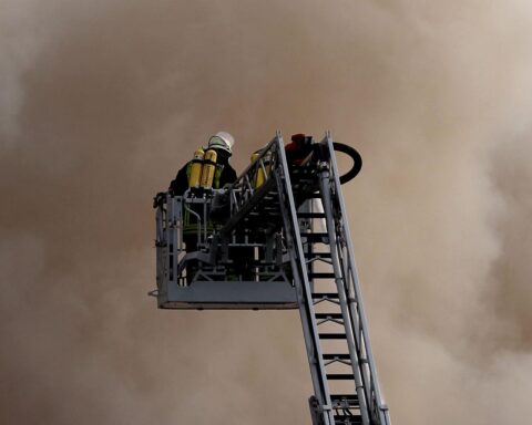 Feuerwehrleute auf einer Drehleiter, Einsatzfahrzeuge am Unfallort, Rettungskräfte leisten Hilfe.