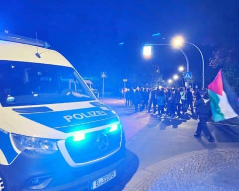 Bunte Demonstranten mit Plakaten, Polizei im Hintergrund, friedliche Atmosphäre, urbaner Kontext in Berlin.