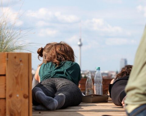 Junge Frau genießt Getränke auf Dachterrasse mit Blick auf Berliner Fernsehturm, sonniges Wetter.