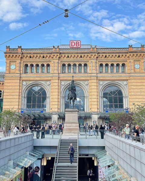Sonniger Hauptbahnhof mit Menschen, umgeben von frühlingshaftem Wetter und klar blauem Himmel.