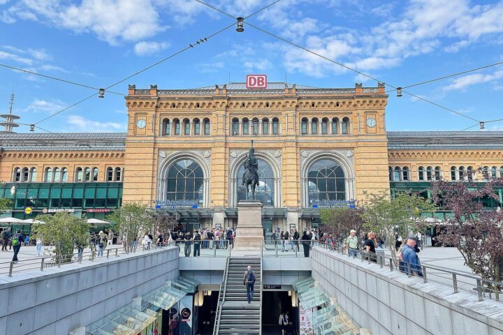 Sonniger Hauptbahnhof mit Menschen, umgeben von frühlingshaftem Wetter und klar blauem Himmel.