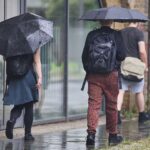 Personen mit Regenschirmen in einer wechselhaften, regnerischen Umgebung, passend zum Wetterbericht.