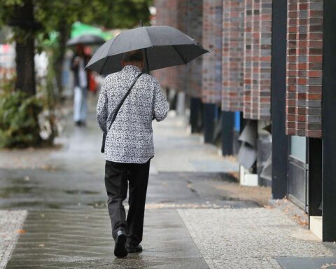 Mann im Regen mit Regenschirm, umgeben von grauem, bewölktem Himmel und nassen Straßen.
