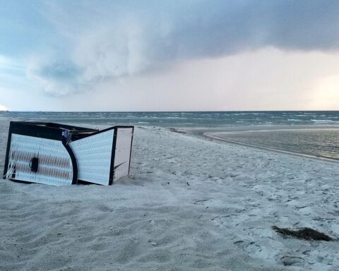 Umgekippter Strandkorb an einem windigen, unbeständigen Strandtag mit Schauern und Gewittern.