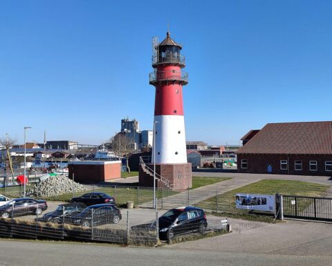 Leuchtturm bei strahlendem Sonnenschein, umgeben von klarem Himmel und ruhigem Meer.