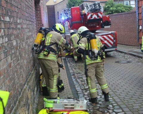Feuerwehrleute löschen Brand im Dachgeschoss eines Mehrfamilienhauses, Unterstützung durch mehrere Einsatzkräfte.