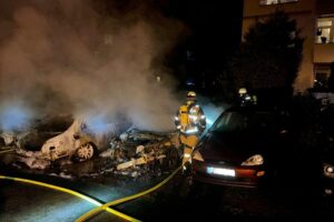 Brandstelle mit zwei ausgebrannten Autos, Feuerwehr im Einsatz zur Brandbekämpfung und Abdämmung.